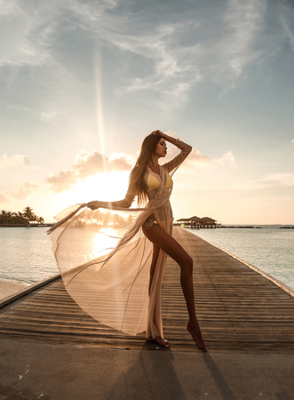 fashion photo of beautiful sexy girl with dark hair in elegant beach clothes, relaxing on Maldive island beachの写真素材