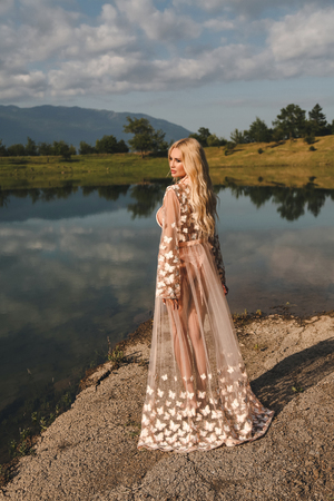 fashion outdoor photo of beautiful sexy woman with blond hair in elegant swimming suit posing in nice nature place, a lake surrounded by mountainsの写真素材
