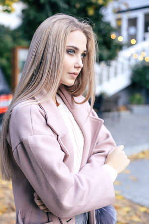 fashion street look of beautiful young woman with long blond hair in elegant clothes walking by the streetの写真素材