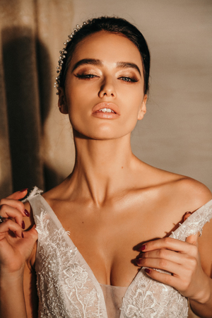fashion photo of beautiful sensual bride with dark hair in luxurious wedding dress and accessories posing in elegant interior of hotelの写真素材