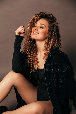 fashion photo of beautiful sexy woman with long blond curly hair in elegant clothes posing in studioの写真素材