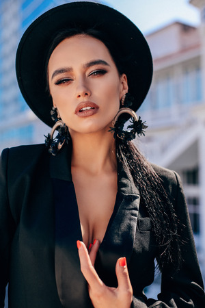 fashion outdoor photo of beautiful sexy woman with dark hair in luxurious clothes and black hat walking by the spring cityの写真素材