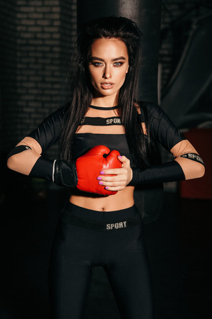 fashion photo of beautiful sexy woman with dark hair in sportive clothes and boxing gloves training in gymの写真素材