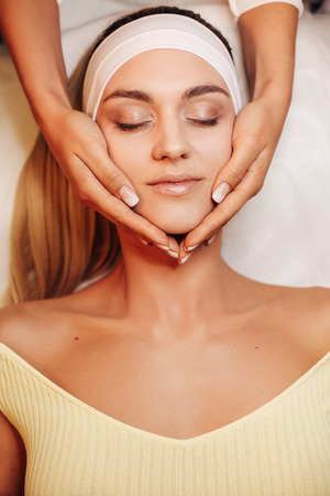 fashion photo of beautiful woman with dark hair and glowing sking making procedure in beauty salonの写真素材