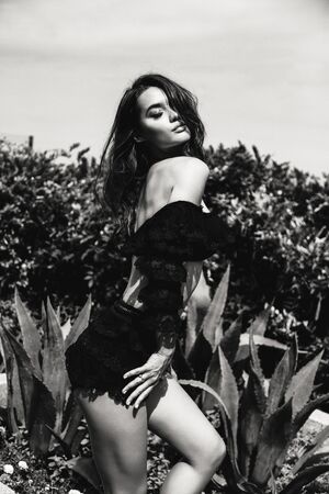 Beautiful sensual woman with dark hair in elegant lace black suit posing in summer parkの写真素材