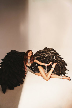 fashion studio photo of beautiful sexy woman with dark hair in elegant lingerie and decorative black wingsの写真素材
