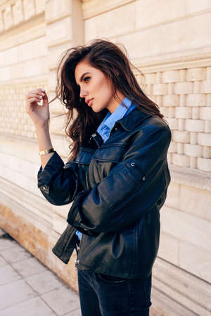 fashion outdoor photo of beautiful woman with dark hair in leather jacket walking on the streetの写真素材