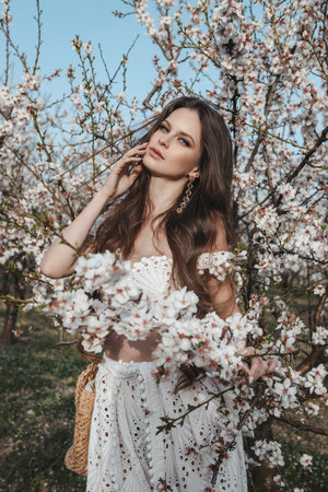 fashion outdoor photo of beautiful woman with dark hair in elegant dress posing in spring blooming gardenの写真素材