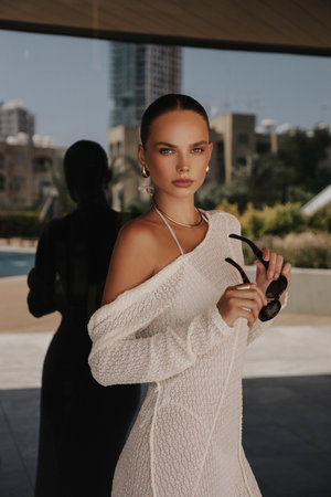 fashion outdoor photo of beautiful woman with dark hair in elegant white dress and accessories posing near mirror window of the hotelの写真素材