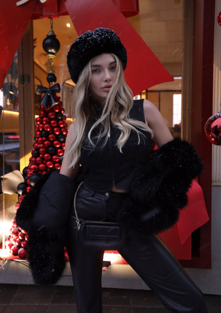 fashion outdoor photo of beautiful woman with blond hair in elegant fur coat and accessories posing near shop window decorated for Christmasの写真素材