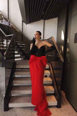 fashion photo of beautiful woman with dark hai in elegant red dress posing in luxury hotel hallの写真素材
