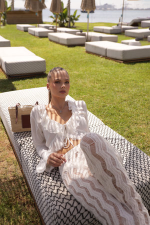 fashion outdoor photo of beautiful woman with dark hair in elegant clothes and accessories relaxing in summer beach clubの写真素材