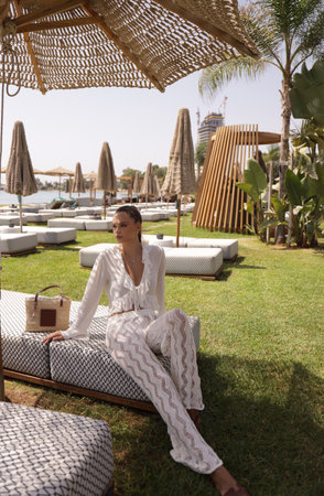 fashion outdoor photo of beautiful woman with dark hair in elegant clothes and accessories relaxing in summer beach clubの写真素材