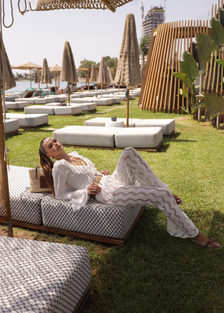 fashion outdoor photo of beautiful woman with dark hair in elegant clothes and accessories relaxing in summer beach clubの写真素材