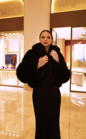 fashion interior photo of beautiful sensual woman with dark hair in luxurious black fur coat and jewelry posing in hall of the hotelの写真素材