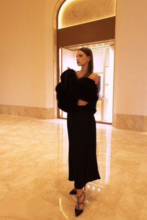 fashion interior photo of beautiful sensual woman with dark hair in luxurious black fur coat and jewelry posing in hall of the hotelの写真素材