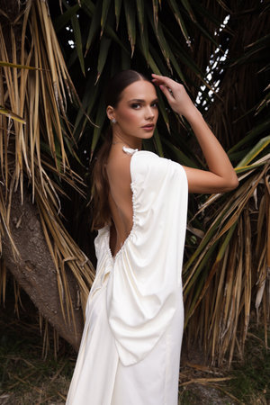fashion outdoor photo of beautiful woman with dark hair in luxurious wedding dress with jewelry posing in beautiful nature place Lefkara, with palm tree in the backgroundの写真素材