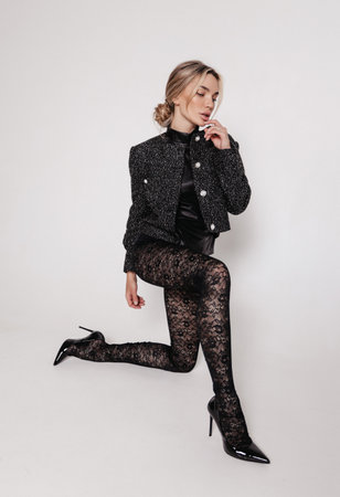 fashion photo of beautiful woman with blond hair in elegant patterned tights and jacket posing in studioの写真素材