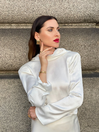 fashion outdoor photo of beautiful woman with dark hair in luxurious white silk dress and accessories posingの写真素材