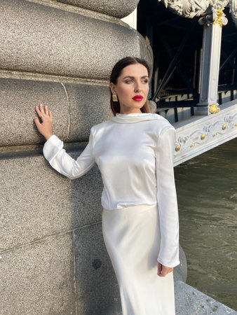 fashion outdoor photo of beautiful woman with dark hair in luxurious white silk dress and accessories posing by the Alexandre III bridge in Parisの写真素材