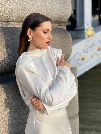 fashion outdoor photo of beautiful woman with dark hair in luxurious white silk dress and accessories posing by the Alexandre III bridge in Parisの写真素材