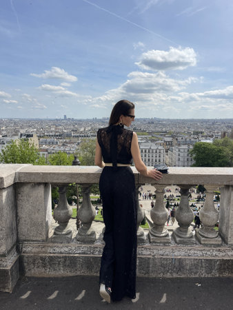 fashion outdoor photo of beautiful woman with dark hair in elegant classic clothes posing on Montmartre with a panoramic view of Parisの写真素材