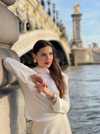 fashion outdoor photo of beautiful woman with dark hair in luxurious white silk dress and accessories posing by the Alexandre III bridge in Parisの写真素材