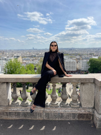 fashion outdoor photo of beautiful woman with dark hair in elegant classic clothes posing on Montmartre with a panoramic view of Parisの写真素材