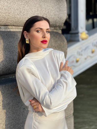 fashion outdoor photo of beautiful woman with dark hair in luxurious white silk dress and accessories posing by the Alexandre III bridge in Parisの写真素材