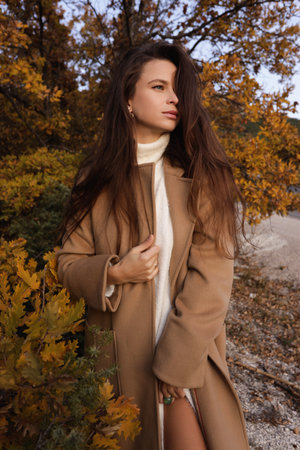 fashion outdoor photo of beautiful woman with dark hair in elegant dress and wool coat posing among beautiful natureの写真素材