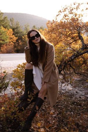 fashion outdoor photo of slavic woman with dark hair in elegant dress and wool coat posing among beautiful natureの写真素材