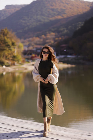 fashion outdoor photo of beautiful slavic woman with dark hair in elegant dress and wool coat posing among beautiful natureの写真素材