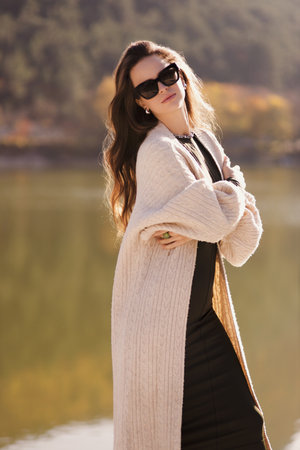 fashion outdoor photo of beautiful woman with dark hair in elegant dress and wool coat posing among beautiful natureの写真素材