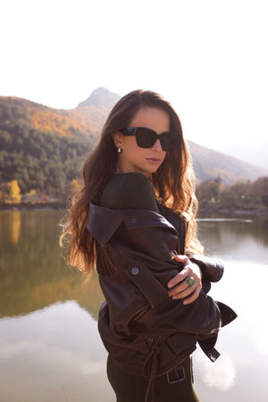 fashion outdoor photo of beautiful slavic woman with dark hair in elegant outfit and jacket posing among beautiful natureの写真素材