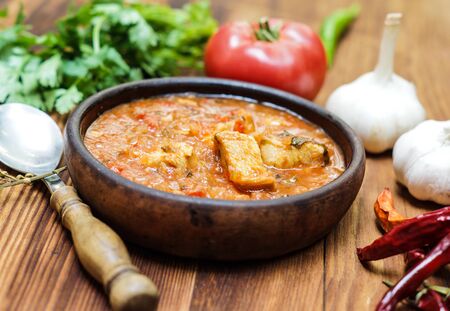 Chakhokhbili - Georgian traditional dish of stewed chicken, tomato with herbsin in a clay bowl on a wooden tableの写真素材