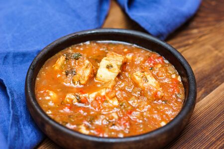 Georgian Chakhokhbili - traditional dish of stewed chicken in a clay bowl on a wooden table decorated with blue napkinの写真素材