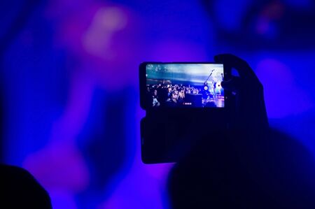 man holds a smartphone over his head and takes off the concertの写真素材