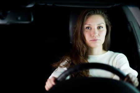 a young girl with her hair holding the steering wheel in a car and looking thoughtfully at the camera. Close-up portraitの写真素材