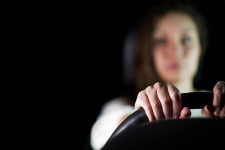 the girl in the background in defocus holds the steering wheel with her hands. Night, the girl in the car is alone, only the hands and the steering wheel are in focusの写真素材