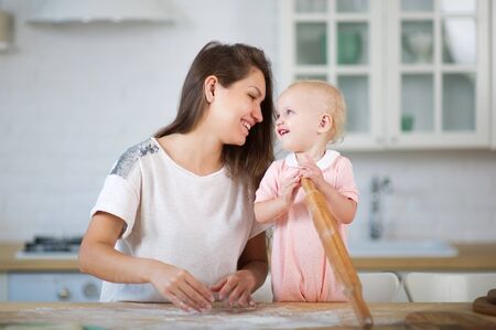 mom and her little daughter are cute looking at each other, playing with flour in the bright kitchenの写真素材