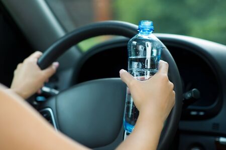 a young girl sits in a car and holds the wheel with one hand and holds a bottle of drinking water with the otherの写真素材