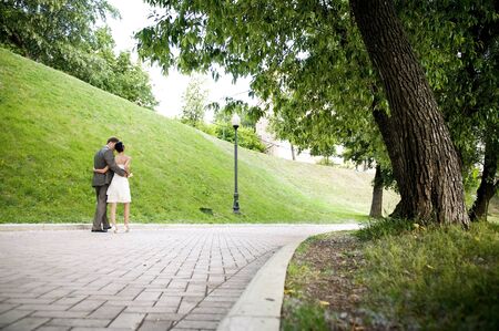 Happy bride and groom are moving away along the alley in the park, huggingの写真素材