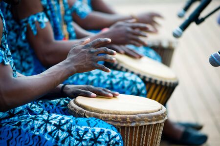 hands of African drummers in blue costumes and traditional drums in front of microphones at a performanceの写真素材