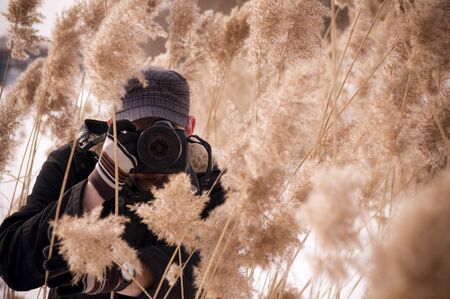 A photographer in a cap, gloves and a dark jacket with a camera takes off from the thicketの写真素材