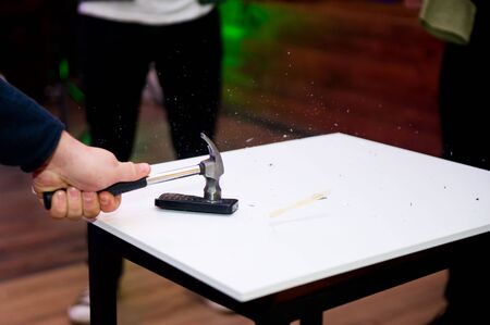 the hammer strikes the old push-button cell phone lying on the table and the fragments fly apartの写真素材