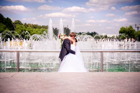 the groom passionately kisses the bride on the background of the fountain behind the chrome railing. faces are turned to each other and the viewer does not see themの写真素材