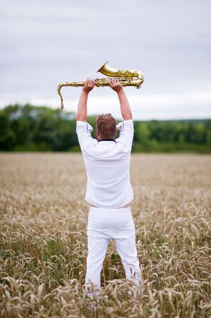 saxophonist in a white suit stands in the field. Flight of the soul, philosophy of freedomの写真素材