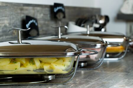 A row of glass dishes with food in the hotel dining room, covered with shiny chrome lidsの写真素材