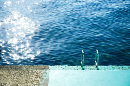 descent into the sea from a concrete slab with a chrome staircase partially painted blueの写真素材