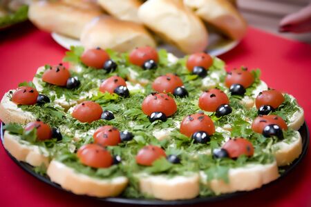 plate with small sandwiches on which there are edible figurines of ladybugs from tomato and olivesの写真素材